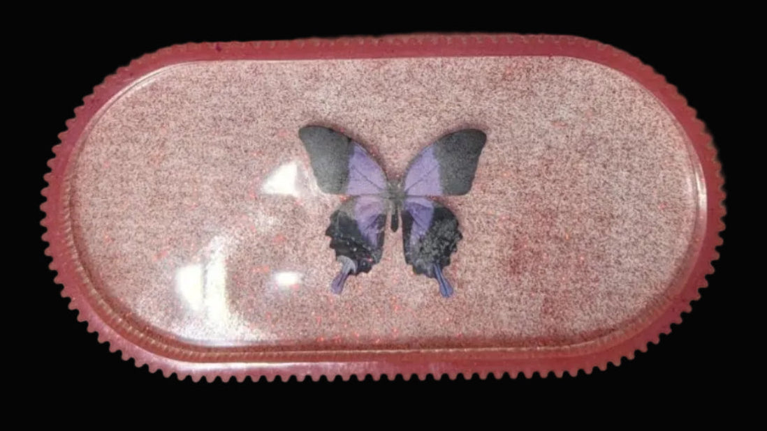 Small pink glitter oval tray with a butterfly in the center set on a white background for visual affect.