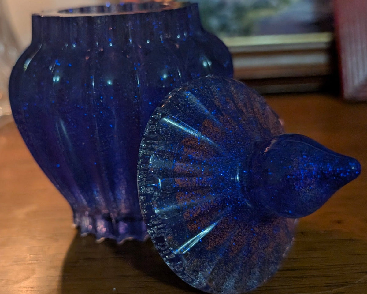 Handcrafted resin vase in a deep, starry blue with a frosted, beveled edge and subtle sparkle throughout. It has a rounded, ribbed body and a matching lid with a rounded finial, giving it an elegant, almost celestial feel. Perfect for adding a touch of handmade charm to any shelf or table.