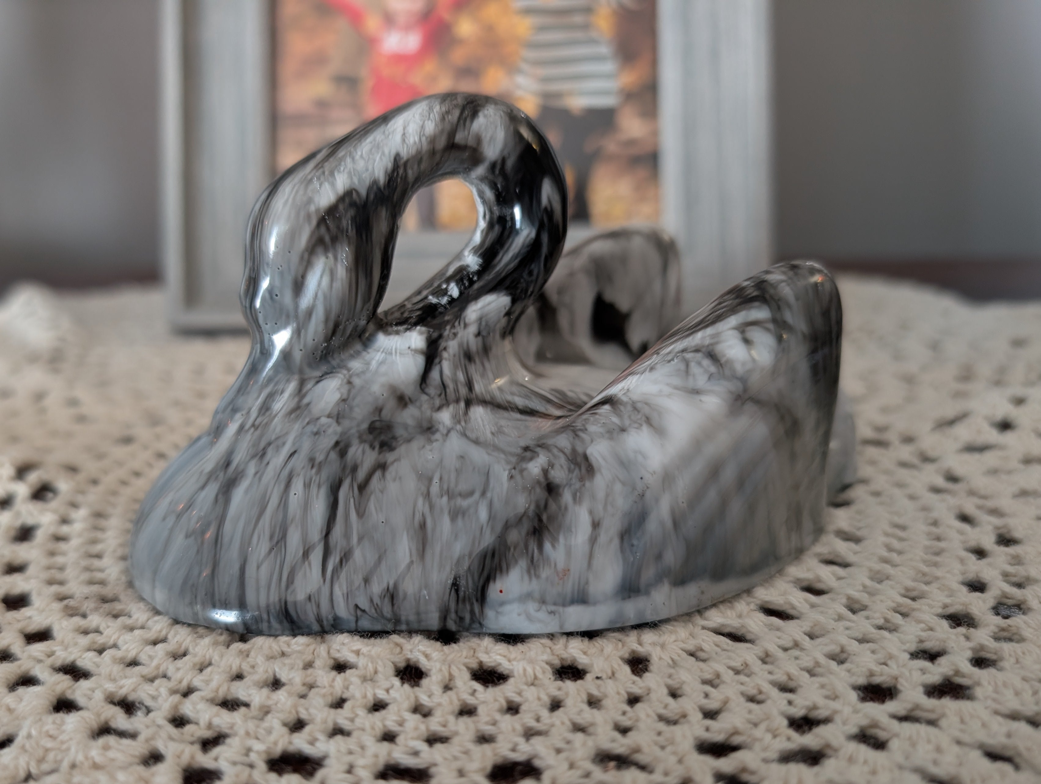 A glossy black and white marbled figurine shaped like a curled-up animal or creature, displayed on a translucent white petal-shaped stand in a tabletop setting.