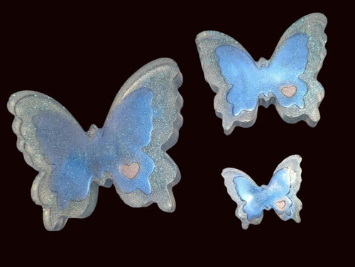 Three butterfly-shaped resin charms in light blue and clear, arranged on a beige fabric surface.