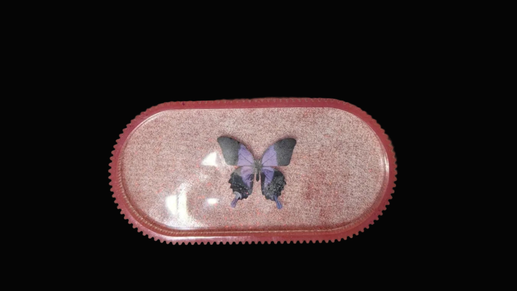 Small pink glitter oval tray with a butterfly in the center set on a white background for visual affect.