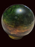A polished iridescent crystal sphere with green, gold, and brown color shifts, sitting on a textured beige tablecloth with other colorful crystal figurines in the background.