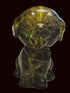 A small translucent green glass figurine of a dog sitting on a beige textured tablecloth, with a red wooden clock and other household items blurred in the background.