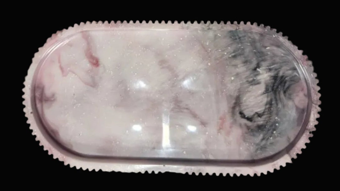 An oval-shaped clear resin tray with a pink and white marble pattern and a textured pink border
